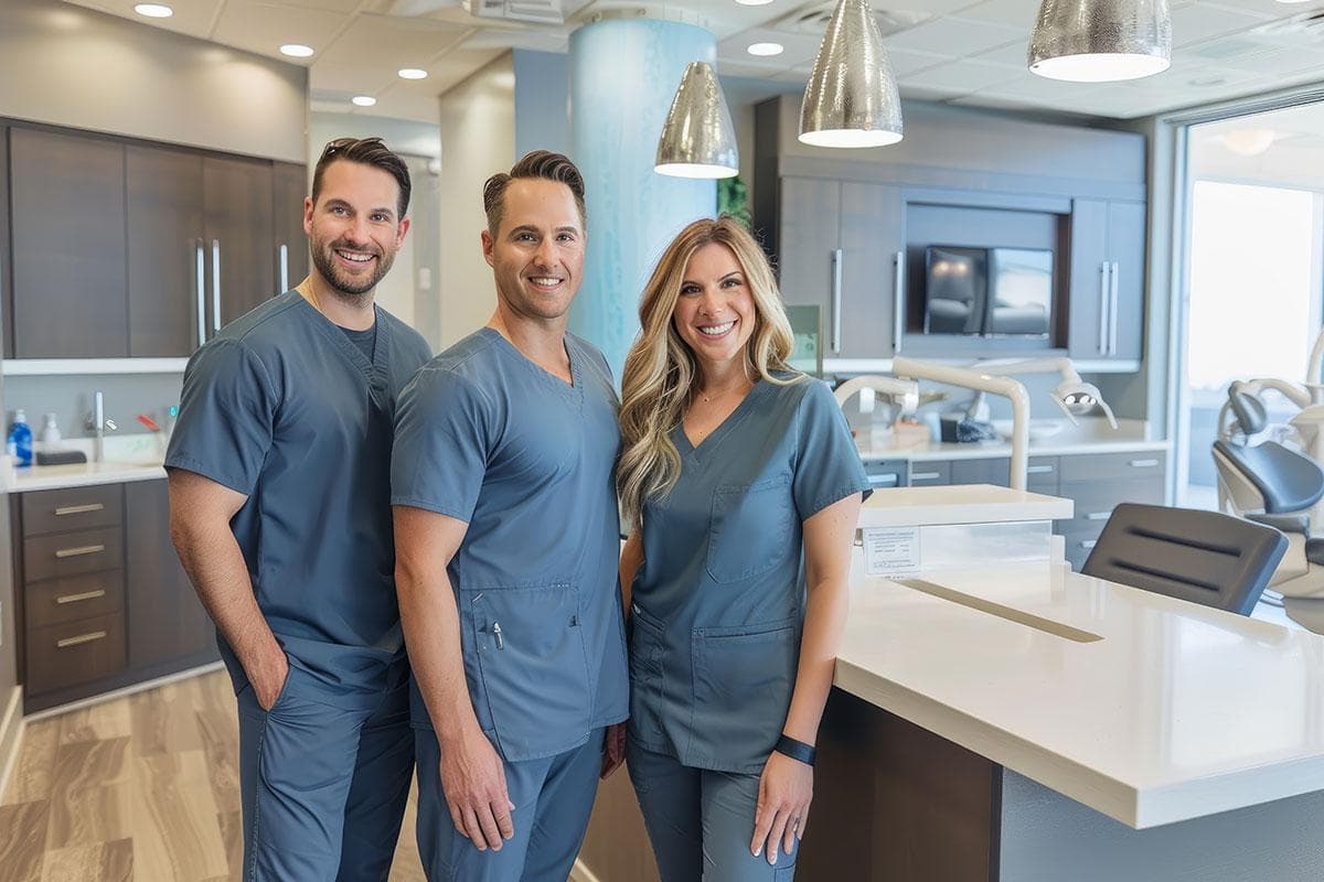 Professional dental team of three healthcare workers in scrubs standing together in a modern dental office