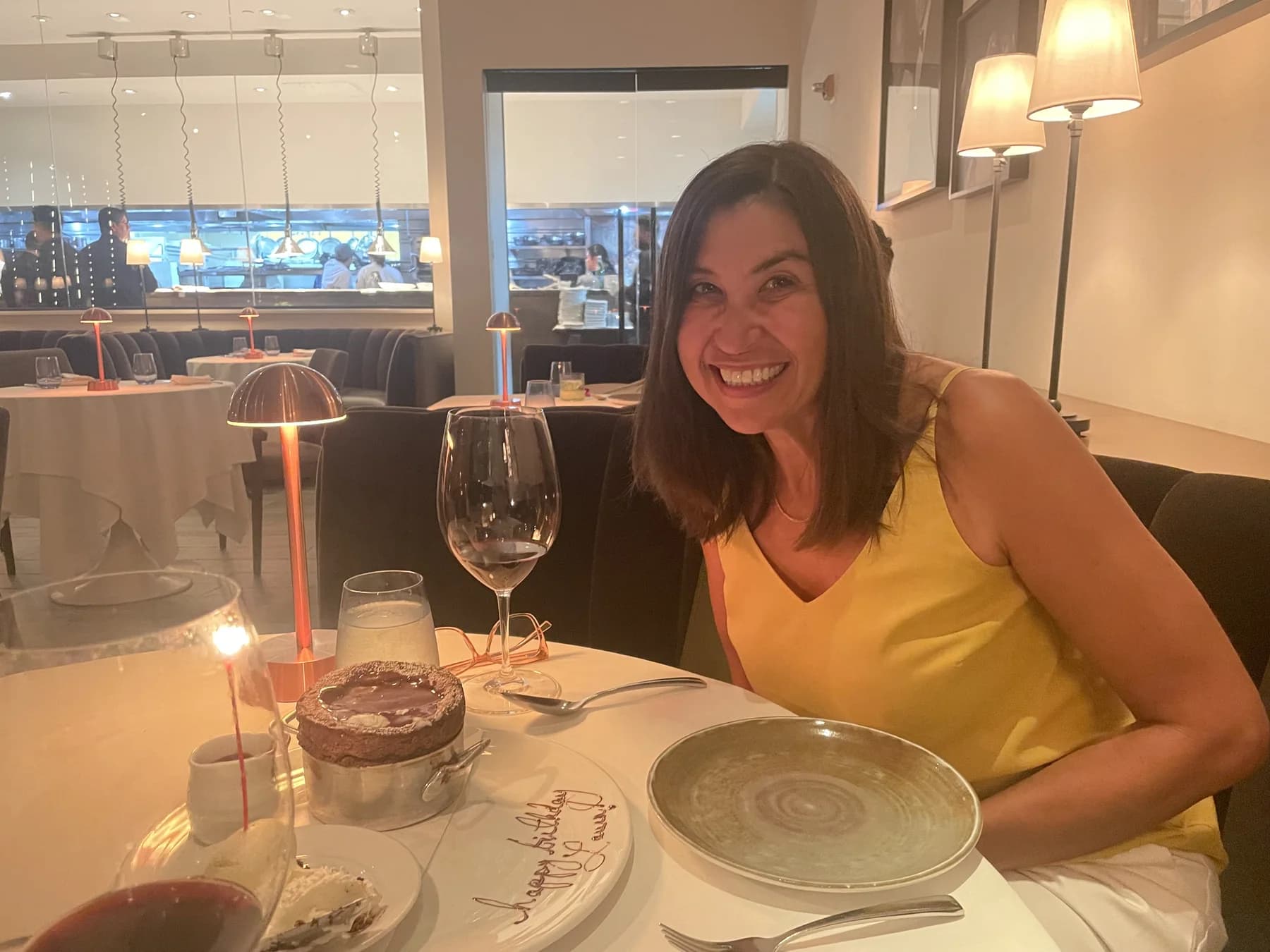 Birthday dinner celebration photo of a woman seated beside dessert in a warmly lit restaurant