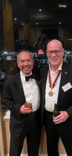 Dr. Michael Njo standing with Dr. Allen Budenz, who is wearing a tuxedo and medallion, at a formal event